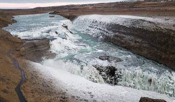 Wide view of a waterfall surrounded by snow-covered cliffs.