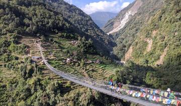 Suspension bridge with people, surrounded by terraced hills.