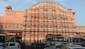 The Hawa Mahal in pink sandstone with cars and people nearby.
