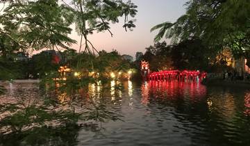Lit-up red bridge over water, surrounded by trees at dusk.