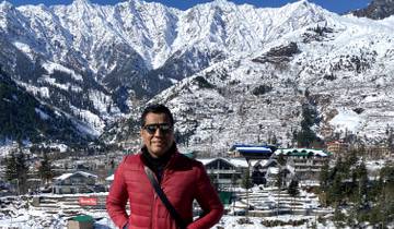 A man posing in front of snow-covered mountains and buildings.