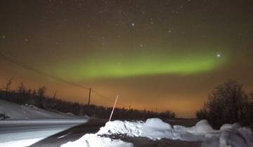 Northern lights in a snowy landscape over a road.