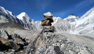 Stones balanced in front of snowy mountain peaks under a clear blue sky.