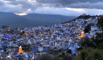 Cityscape of Chefchaouen with colorful buildings and cloudy sky.