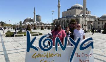 Three people in front of Konya city sign and mosque.