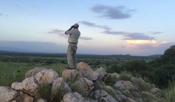 A person standing on rocks, looking through binoculars over a vast landscape.