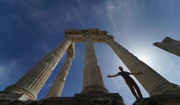 Person standing beside tall ancient columns against a blue sky.