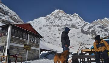 Two people sitting outside a mountain lodge with snow-covered peaks