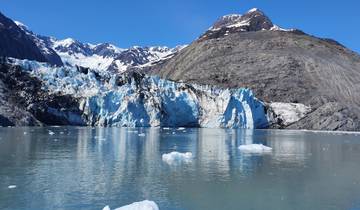 Glacier meeting the sea with snow-capped mountains.