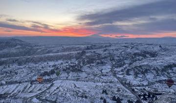 Scenic landscape of Cappadocia with hot air balloons and snowy mountains at sunset.