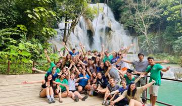 Large group posing exuberantly in front of waterfall.