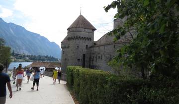 People walking towards a stone castle by a lake