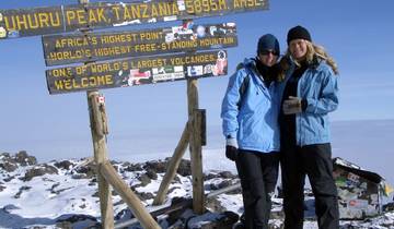 Two people at a mountain summit beside a sign for Uhuru Peak.