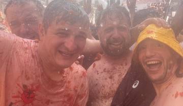 Smiling group of people covered in tomatoes.