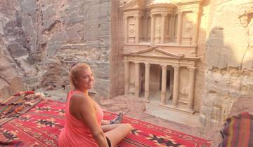 A woman sitting on a carpet overlooking the Petra Treasury.