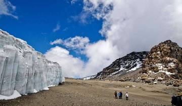 Glaciers and rocky formations under a blue sky, with people hiking.