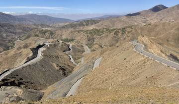 Winding mountain road amidst rocky terrain and vast landscapes.