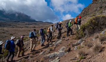 Hikers walking in a mountainous area with clouds overhead.
