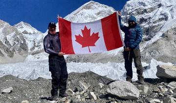 Two people with a Canadian flag in front of mountains at Everest Base Camp.
