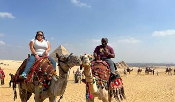 People riding camels with pyramids in the background.