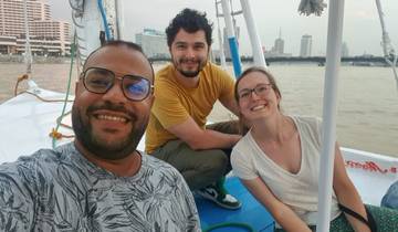 Three people smiling on a boat with a city skyline in the background.