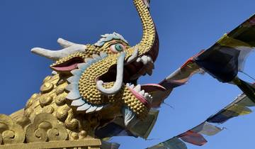 A decorative dragon head with prayer flags under a blue sky.