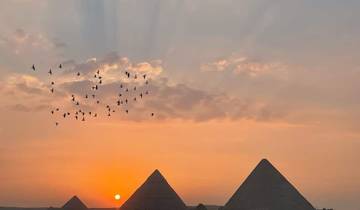 Silhouette of pyramids with birds flying at sunrise.