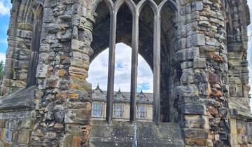 Stone ruins with flowers and a building in the background.