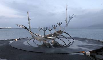 Stainless steel sculpture resembling a ship by the sea.