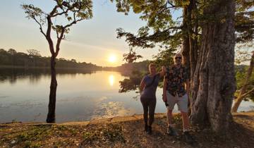 Two people standing by a serene body of water during sunset.