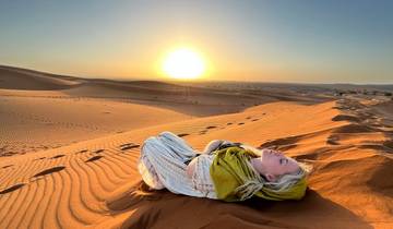 Person lying on sand dunes with sunset in the background.