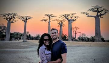 Couple in front of baobab trees at sunset.