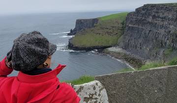 Person with a hat overlooking cliffs and ocean.