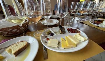 A selection of cheeses and dried fruits on a plate with multiple wine glasses on a table.