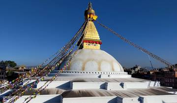 Boudhanath Stupa with prayer flags against a clear blue sky.