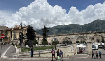Historical town square with stone arches and mountains.