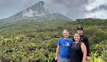 Three people posing in front of a volcano, lush landscape.