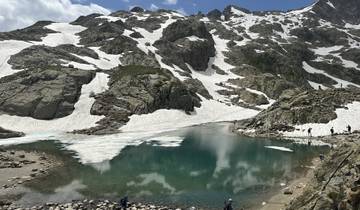 A lake surrounded by snowy mountains with some people around.