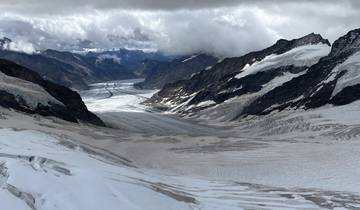 Expansive view of a glacial valley with snow and clouds.