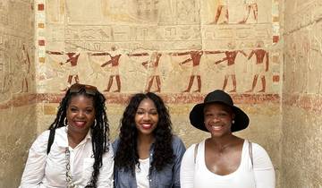 Three people smiling indoors with ancient wall carvings.