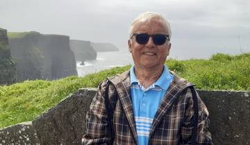 Man in front of Cliffs of Moher with ocean and grassy cliffs in background.