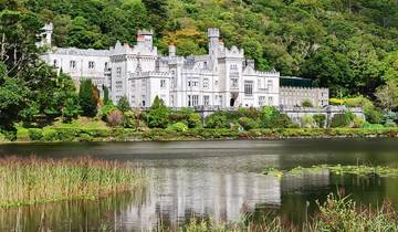 Kylemore Abbey reflecting in a calm lake surrounded by trees.