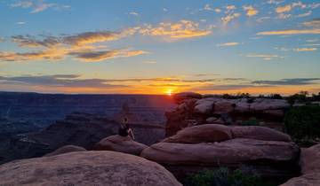 Person sitting on rocks enjoying the sunset view over a canyon.