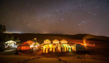 Nighttime view of a desert camp with tents illuminated under a starry sky.