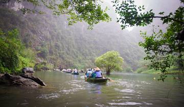 Group of tourists rowing boats in a lush green waterway surrounded by cliffs.