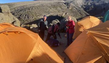 Three people standing near bright tents set up on a rocky surface.