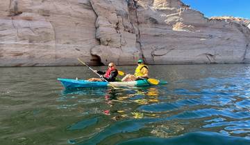 Two people kayaking on a clear blue lake surrounded by rocky cliffs.