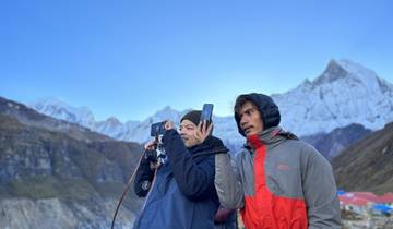 Two people capturing a view of snow-capped mountains.