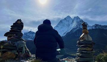 Person sitting between stone cairns with mountain backdrop.