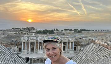 A woman smiling with ancient ruins in the background at sunset.